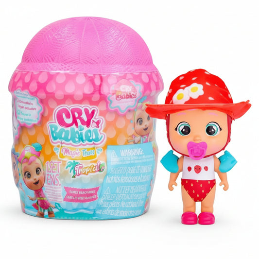 Bambola Cry Babies Magic Tears della serie Tropical con cappellino rosso a pois bianchi, costume da bagno e braccioli celesti, accanto alla confezione a forma di capsula rosa
