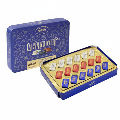 Scatola in blu e oro Feletti I Classici Gianduiotti aperta con assortimento di cioccolatini incartati nei colori bianco, rosso e blu su sfondo bianco