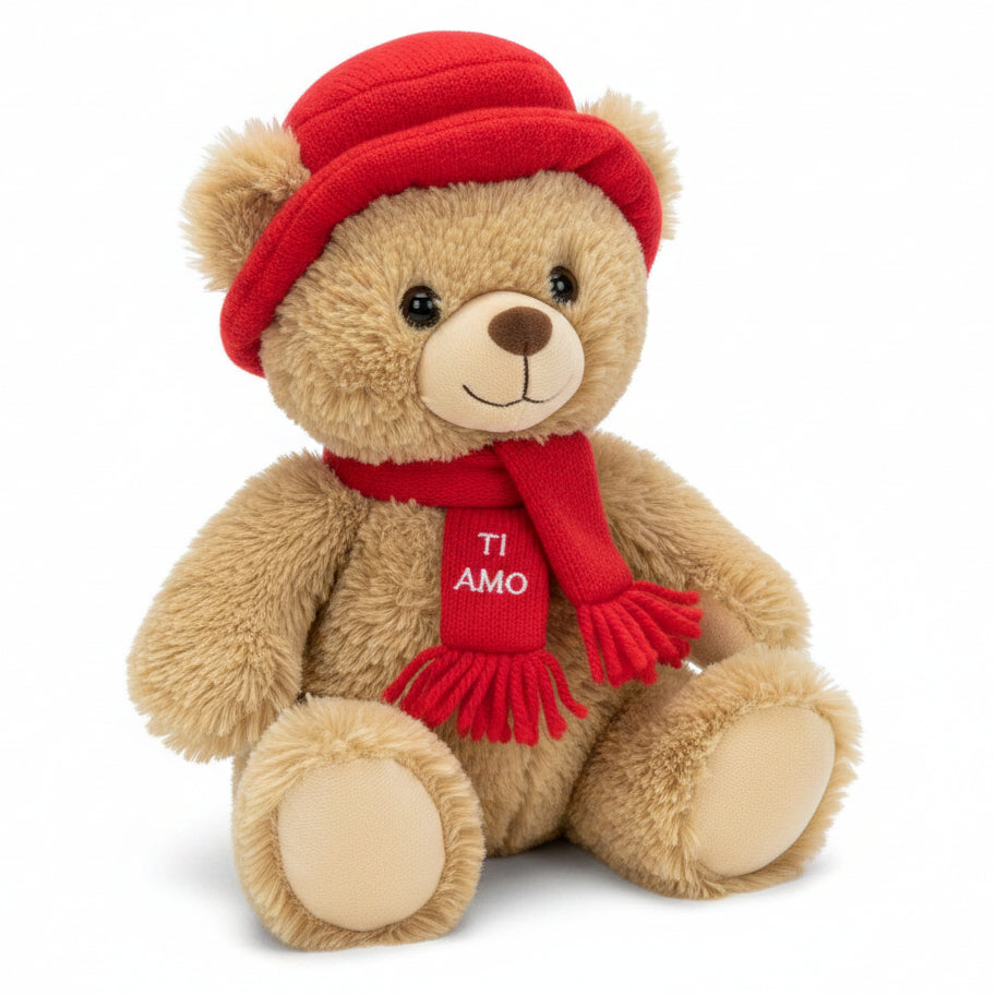 Tenero orsetto di peluche marrone chiaro seduto con cappello e sciarpa rossa con la scritta ricamata Ti Amo su sfondo bianco