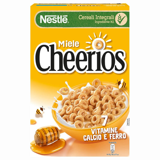 Confezione di cereali Nestlé Cheerios al miele, mostrata con una ciotola di cerchietti nel latte e un mestolo con miele colante su sfondo neutro