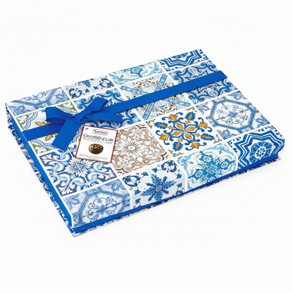 Confezione regalo quadrata Sorini con fantasia di maioliche blu e bianche, decorata con un nastro e un fiocco in tessuto blu su sfondo bianco