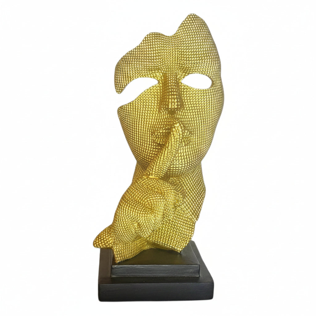 Scultura di design moderno raffigurante una testa dorata con il dito sulle labbra nel gesto del silenzio, poggiata su base nera su sfondo bianco